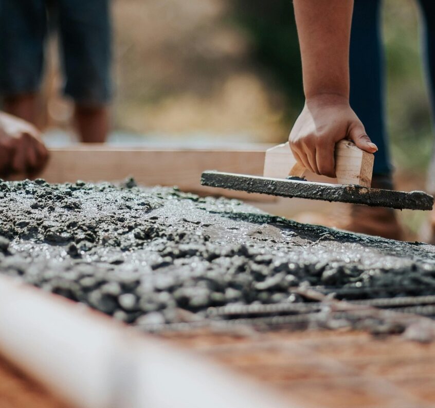 Workers smoothing wet concrete with a trowel on a construction site.