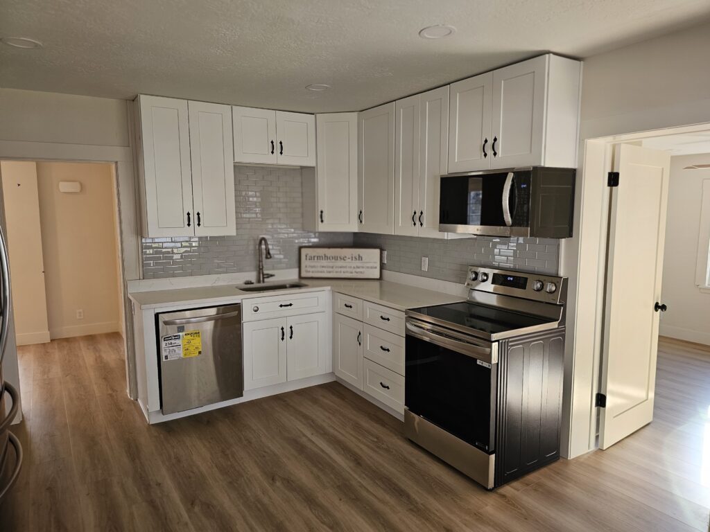 Newly remodeled kitchen with white cabinets, stainless steel appliances, and hardwood floors, reflecting modern home design styles and custom home renovation.