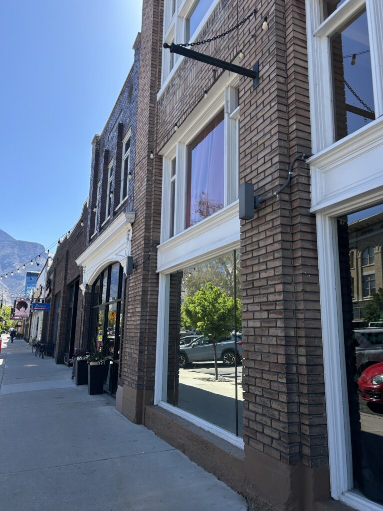 Renovated two-story brick commercial building with large display windows and string lights on a downtown Provo street
