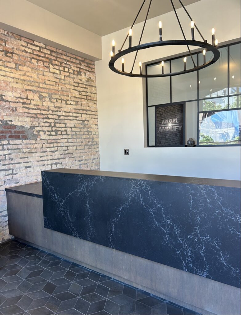 Modern reception area with a black marbled desk, exposed brick wall, and tile floors, perfect for remodeling inspiration.