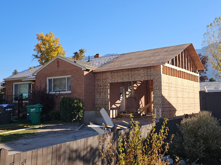 Residential Construction: Brick ranch home with new wood-framed addition under construction showing sheathing and open wall framing