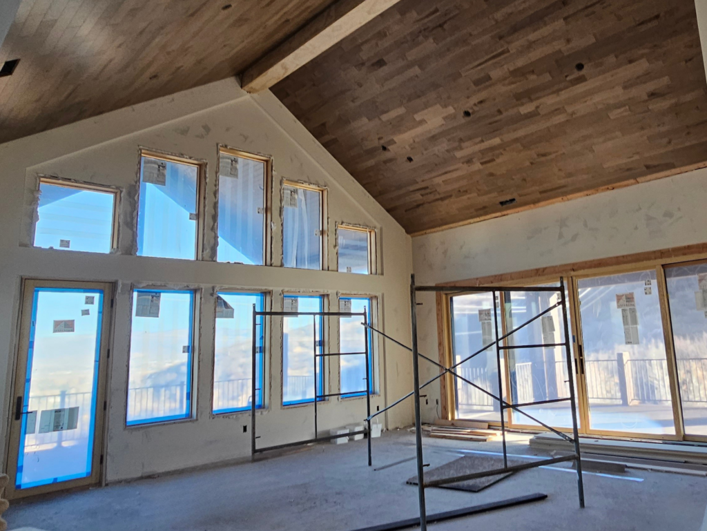Interior of a custom home under construction with vaulted wood plank ceilings, large windows, and scaffolding, highlighting the craftsmanship behind custom home plans and residential engineering services.