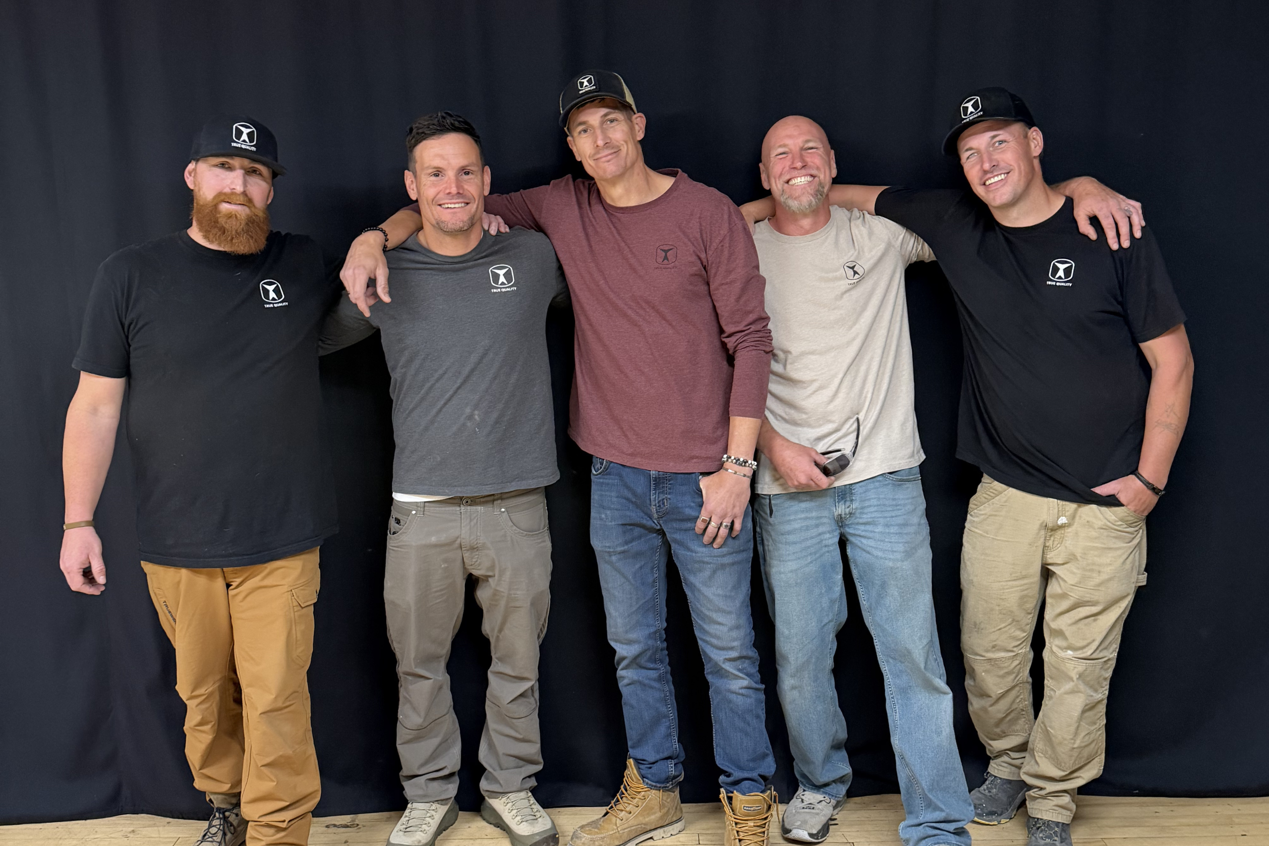 True Quality Construction's team of five smiling together, wearing branded company shirts, representing their experienced residential and concrete construction crew.