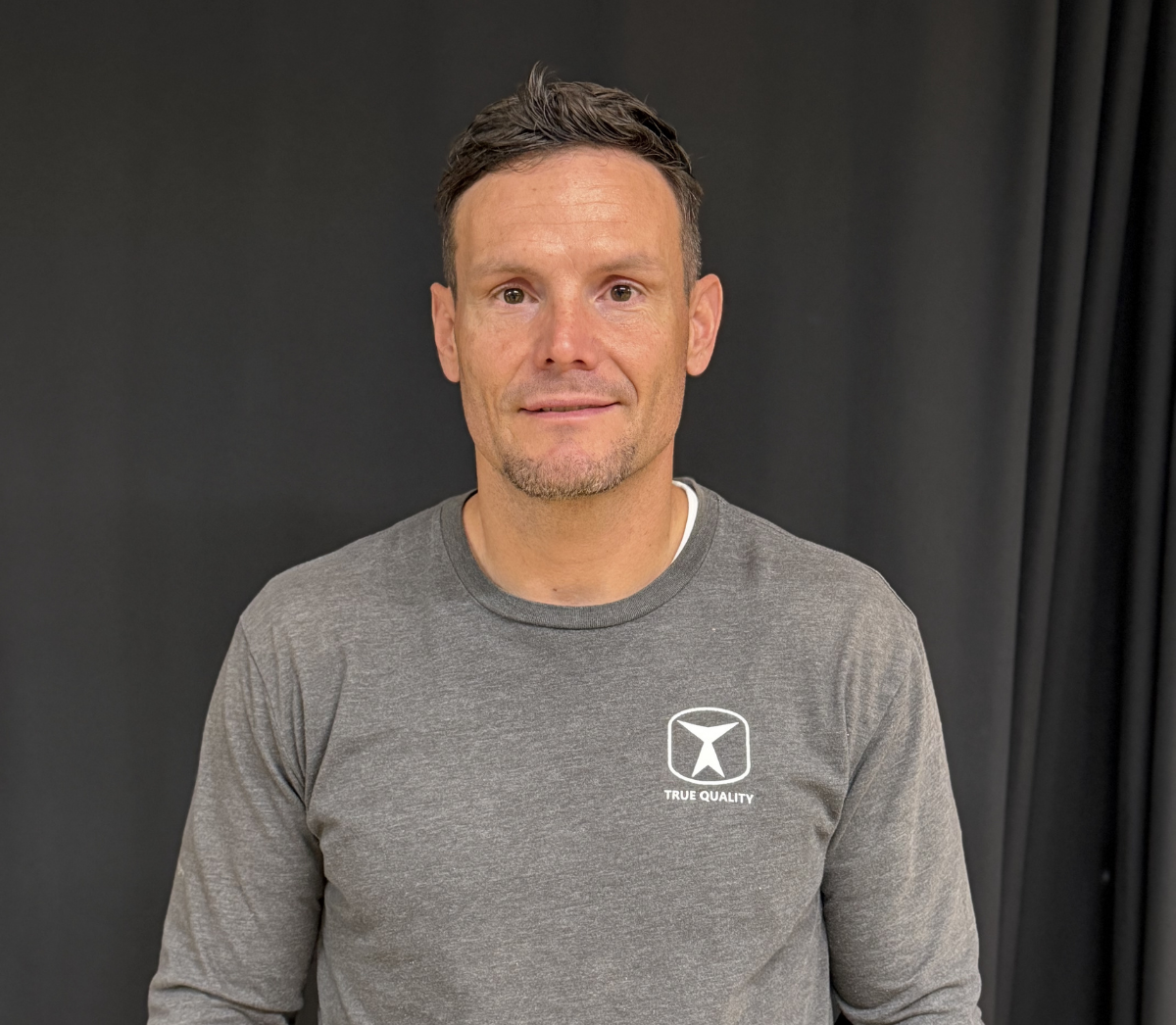 True Quality Construction CEO smiling in a branded company shirt, representing the experienced leadership behind the company's residential and concrete construction services.