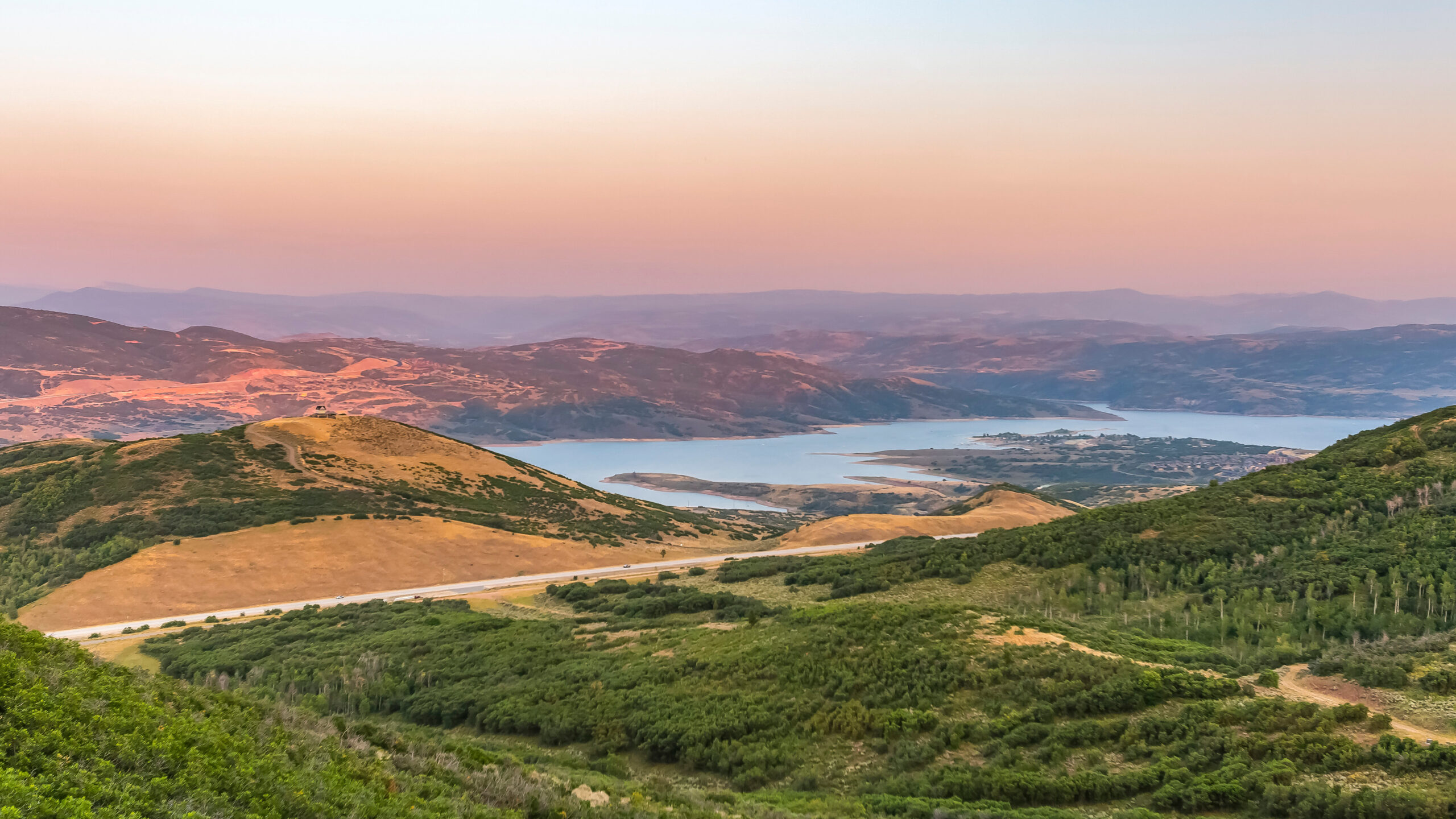 Scenic view of rolling green hills and a lake at sunset