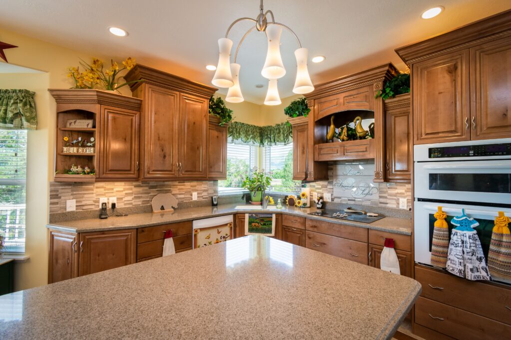 Country kitchen with wood cabinetry, granite countertops, tile backsplash, and a chandelier over the island.