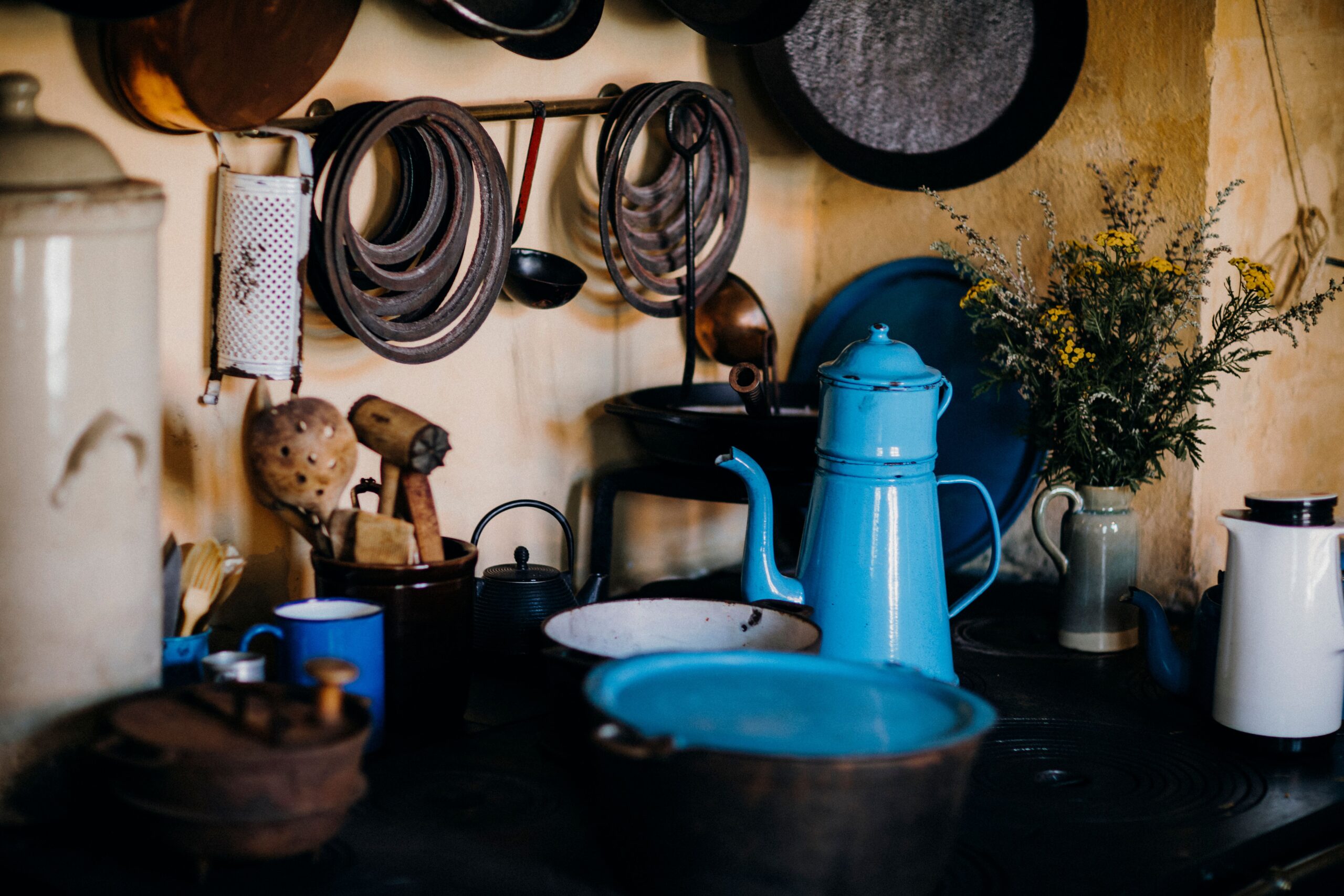 Rustic country kitchen corner with a blue enamel pitcher and basin, coiled ropes hanging on a weathered wall.