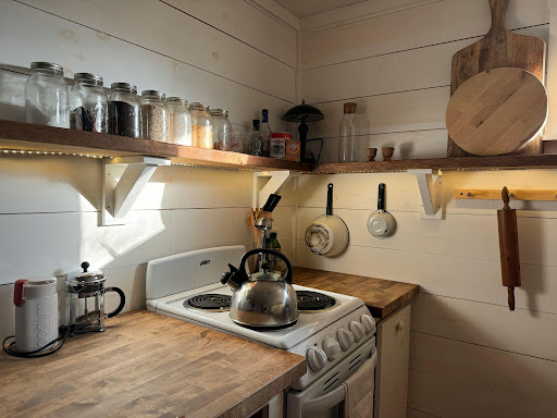 Cozy farmhouse kitchen with shiplap walls, open shelving lined with mason jars, butcher block counters, and a vintage stove.