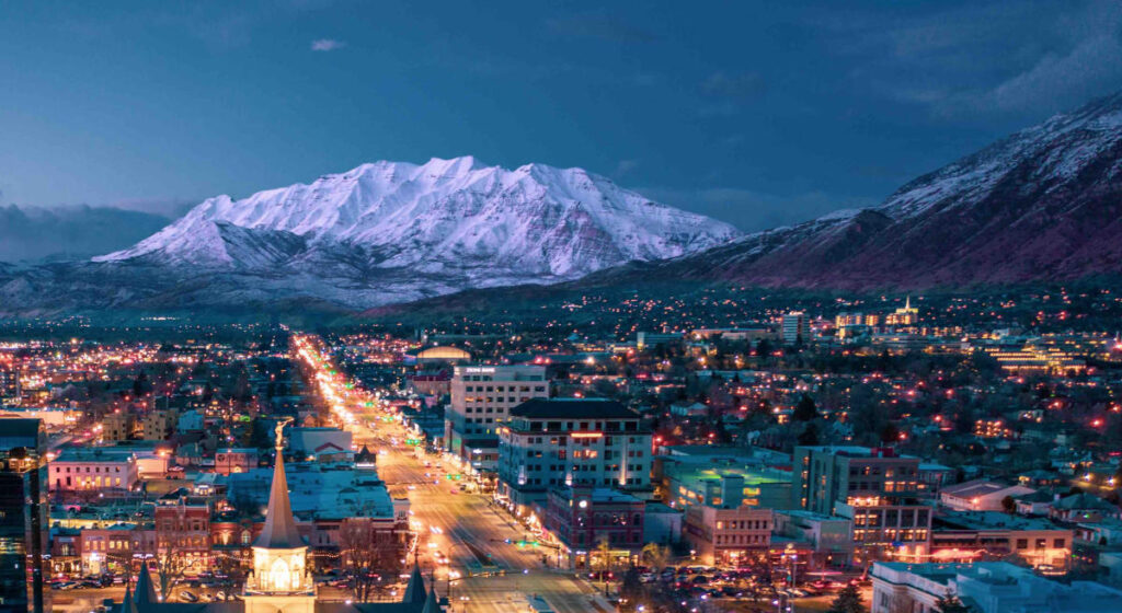Aerial night view of downtown Provo, Utah County with snow-capped Mount Timpanogos in the background