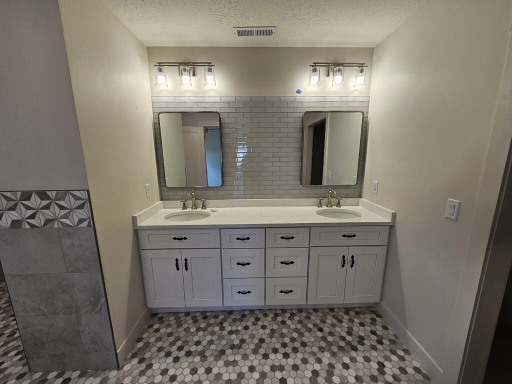 Bathroom with a white double vanity, two round mirrors, gold faucets, and hexagon tile flooring.