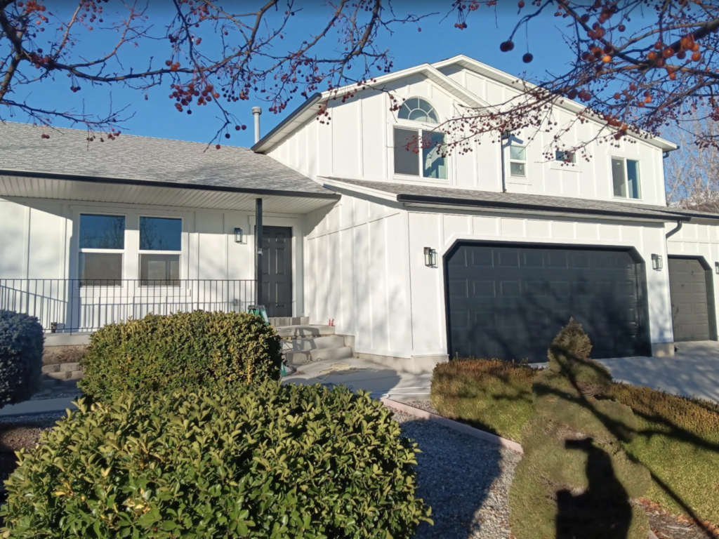 White two-story house with dark garage doors, a covered front porch, and landscaped bushes along the walkway.
