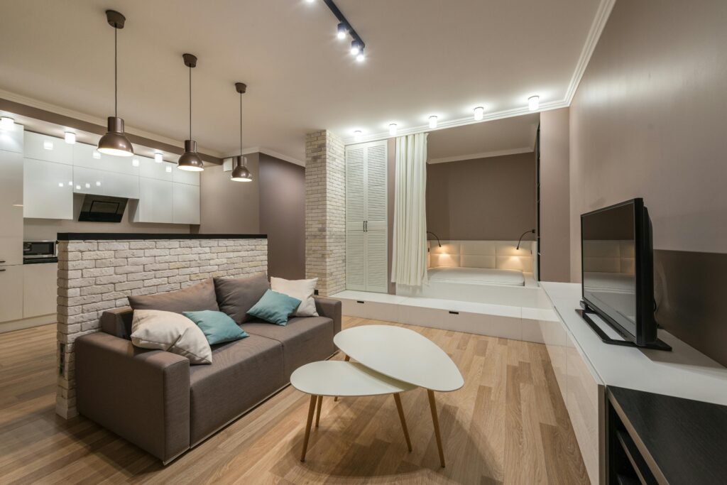 Finished basement apartment with open living area, brick accent wall, pendant lights, and built-in sleeping nook