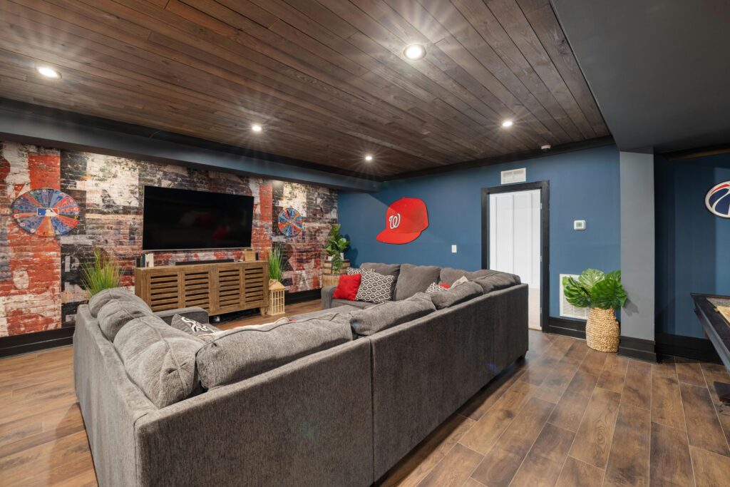 Finished basement entertainment room with sports-themed accent wall, large sectional, and wood plank ceiling